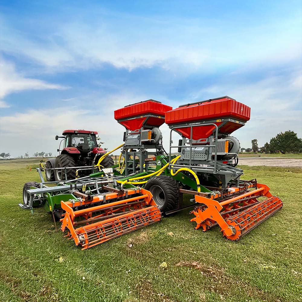 Configuración agrícola con dos kits Altina livianos montados sobre implementos de arrastre, conectados a un tractor en campo abierto. La imagen muestra los equipos con tolvas rojas, tubos de distribución amarillos y rodillos anaranjados listos para labores de siembra o fertilización.